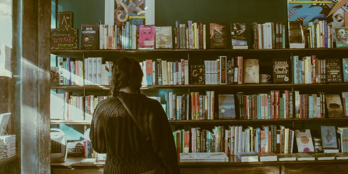 A person thoughtfully browsing a collection of books, deciding on their next read.