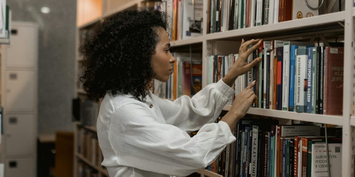 A person intently browsing a diverse collection of books in a library or bookstore.