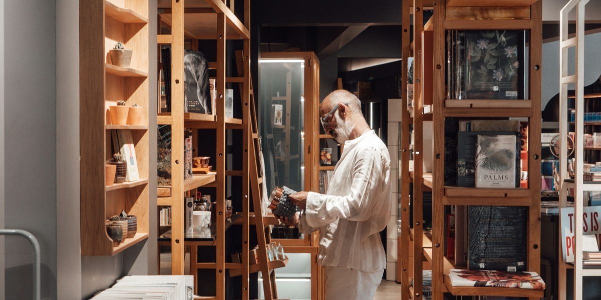 A person navigating a library aisle, pondering over numerous book choices, reflecting the challenge of picking a new series.